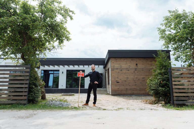 Real estate agent standing outside modern house with for sale sign, featuring contemporary design.